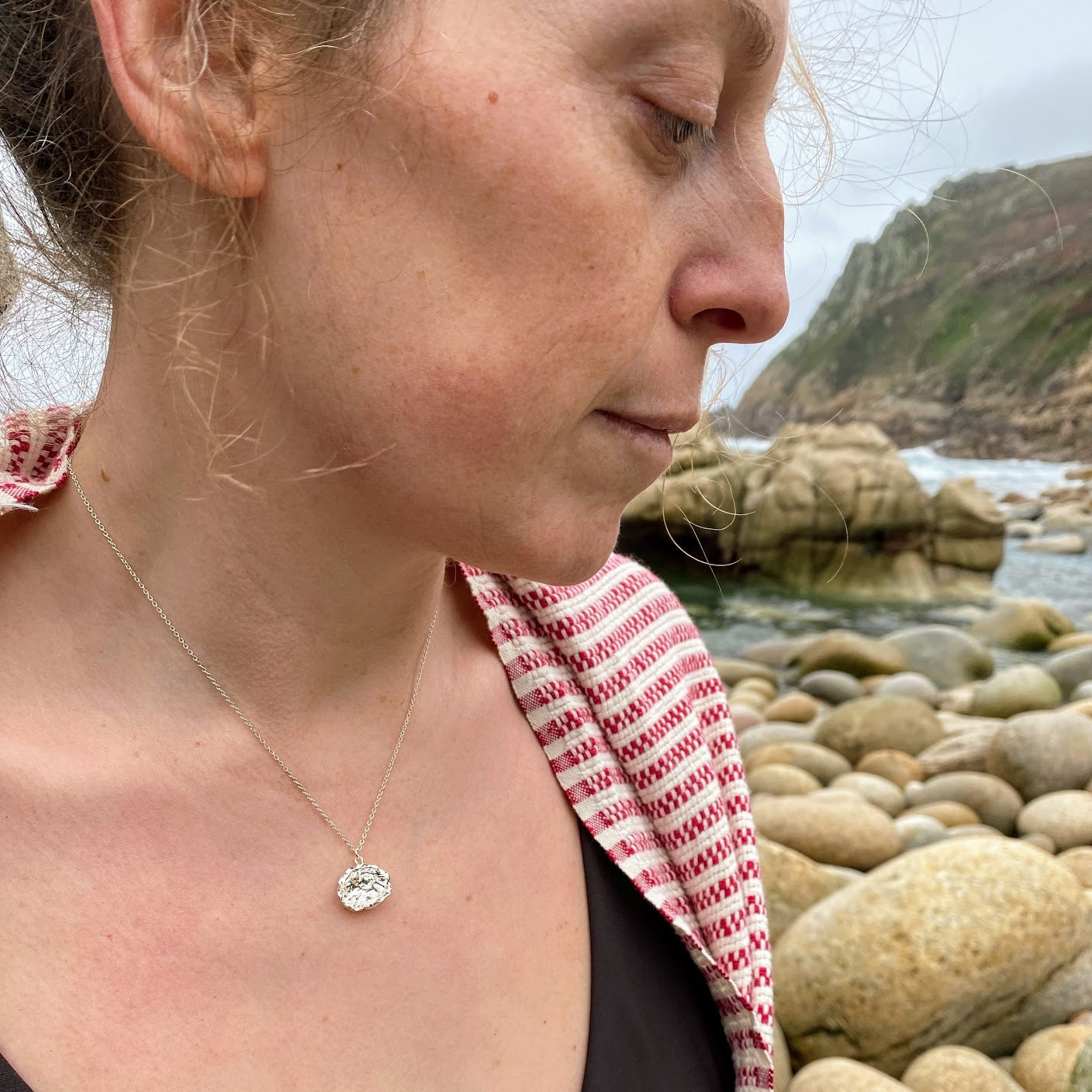 Imagine a stunning sterling silver pendant inspired by the sea, featuring a natural texture and charming organic shape. Crafted by pouring molten silver into the sea, its unique form captures the essence of ocean waves. As sunlight dances upon it, the pendant comes alive, showcasing its intricate details and textures. Picture it photographed on a picturesque beach in Cornwall, close to where it was lovingly created.