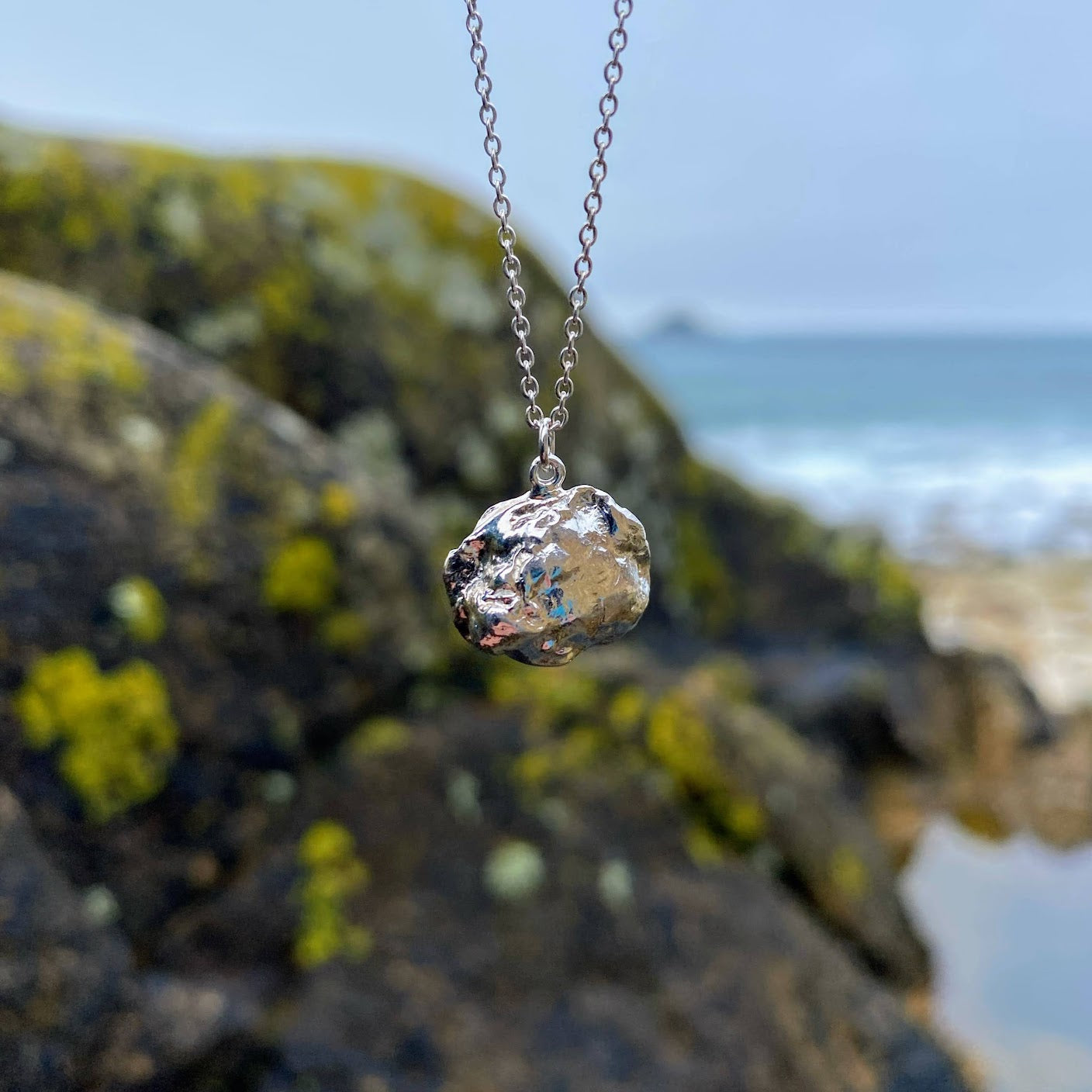 Imagine a stunning sterling silver pendant inspired by the sea, featuring a natural texture and charming organic shape. Crafted by pouring molten silver into the sea, its unique form captures the essence of ocean waves. As sunlight dances upon it, the pendant comes alive, showcasing its intricate details and textures. Picture it photographed on a picturesque beach in Cornwall, close to where it was lovingly created.