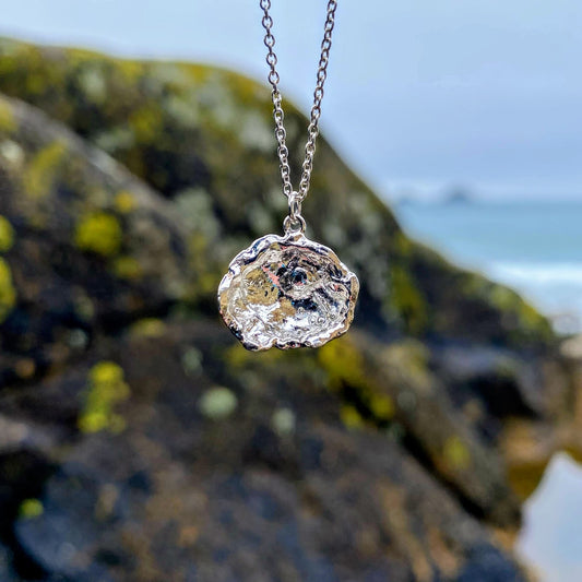 Imagine a stunning sterling silver pendant inspired by the sea, featuring a natural texture and charming organic shape. Crafted by pouring molten silver into the sea, its unique form captures the essence of ocean waves. As sunlight dances upon it, the pendant comes alive, showcasing its intricate details and textures. Picture it photographed on a picturesque beach in Cornwall, close to where it was lovingly created.